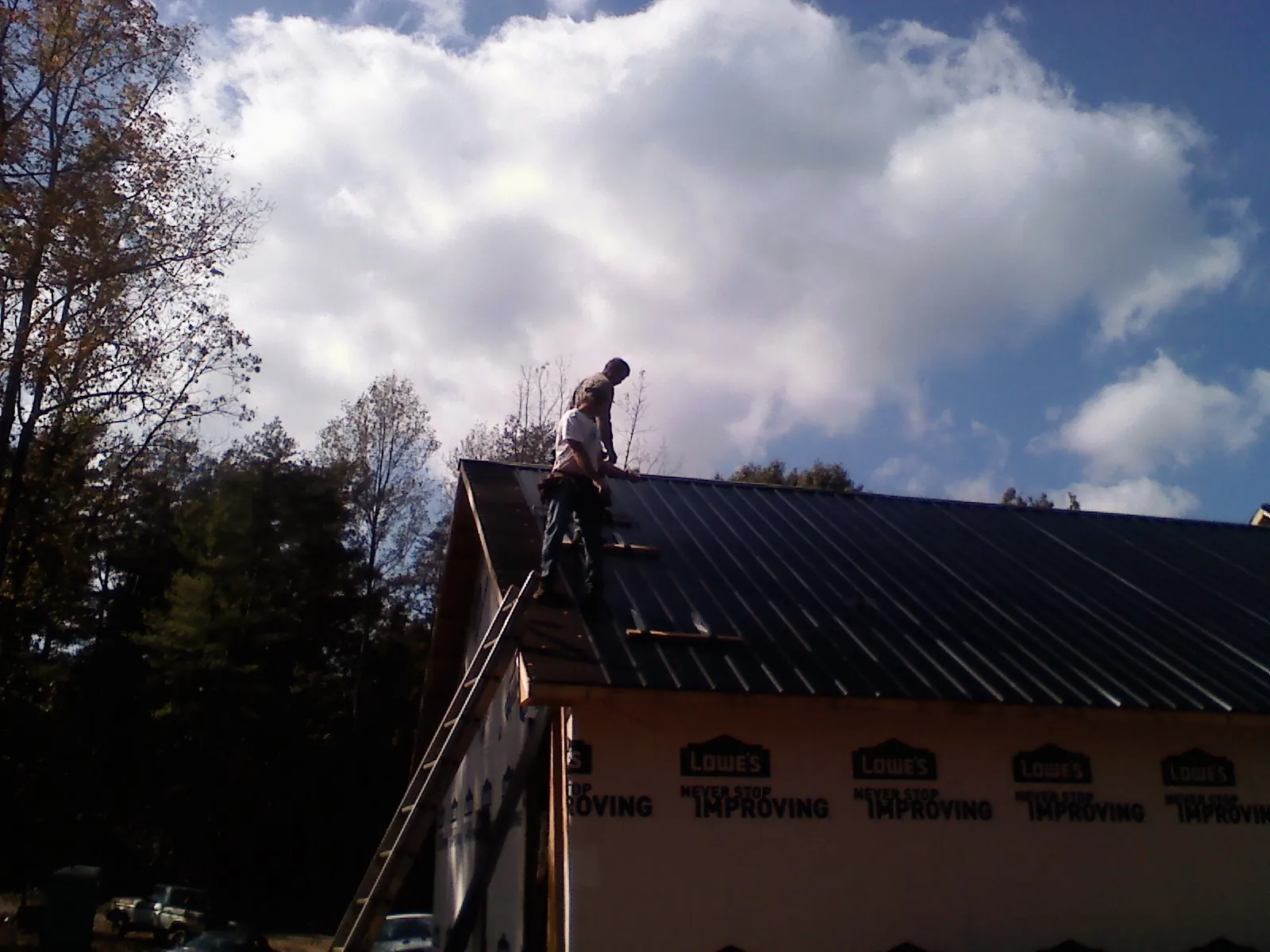 Roofer fastening dark metal panels high against a cloudy sky, from a Roof Inspection job in Bethune