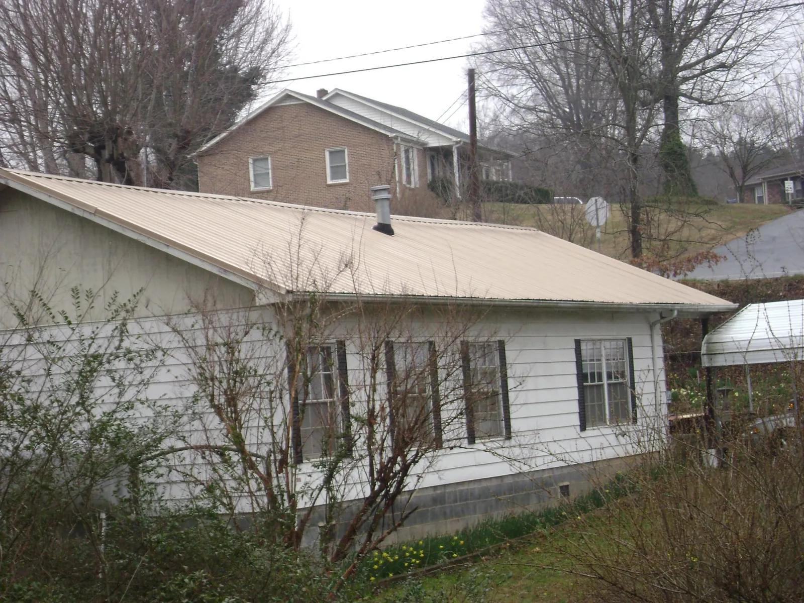 Tan metal roof on a white sided house set into a hillside — Commercial Roofing by Roofing Brothers in Bethune