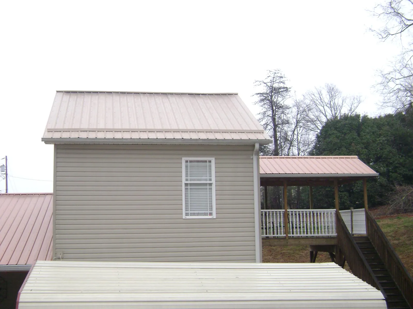 Tan metal roofs on a two story addition and attached porch, from a Roof Replacement job in Bethune